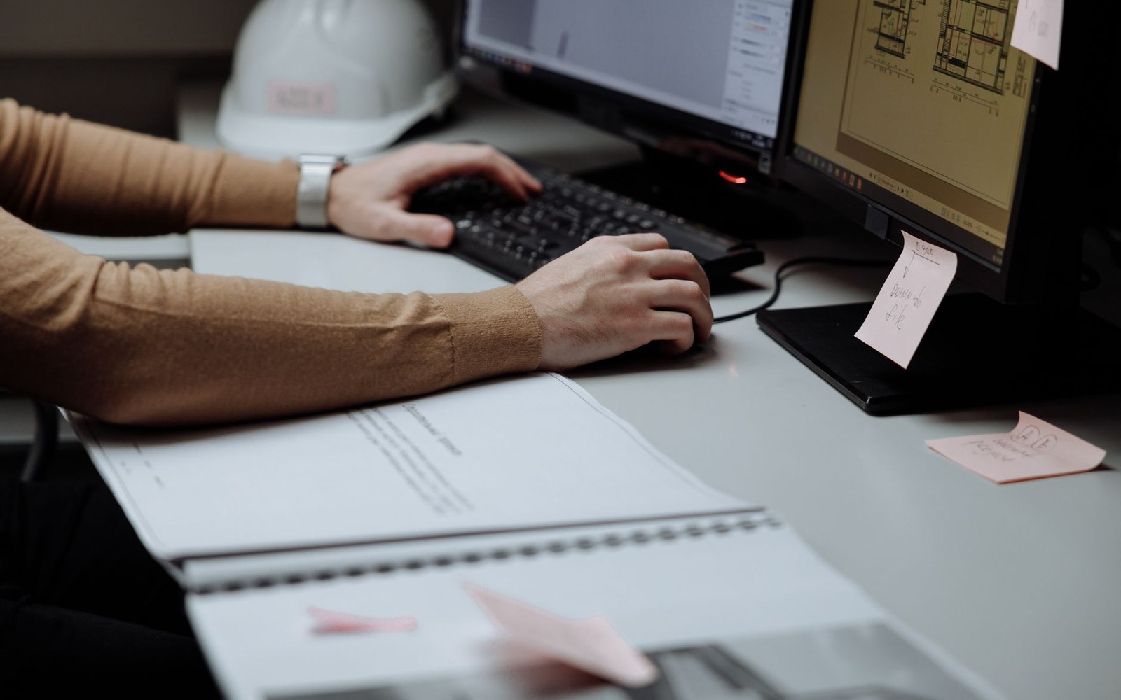 A picture desk with two monitors: one showing a stock library browser, the other a legal document, adult hands at the keyboard, overhead office light
